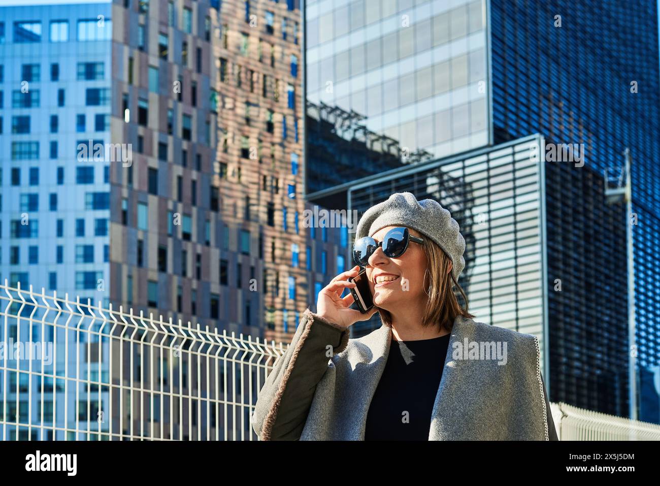 Donna gioiosa che parla al telefono, sfondo urbano moderno Foto Stock