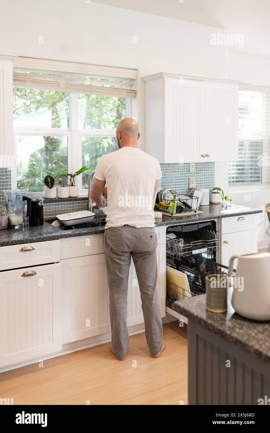 Uomo che fa piatti in cucina soleggiata Foto Stock