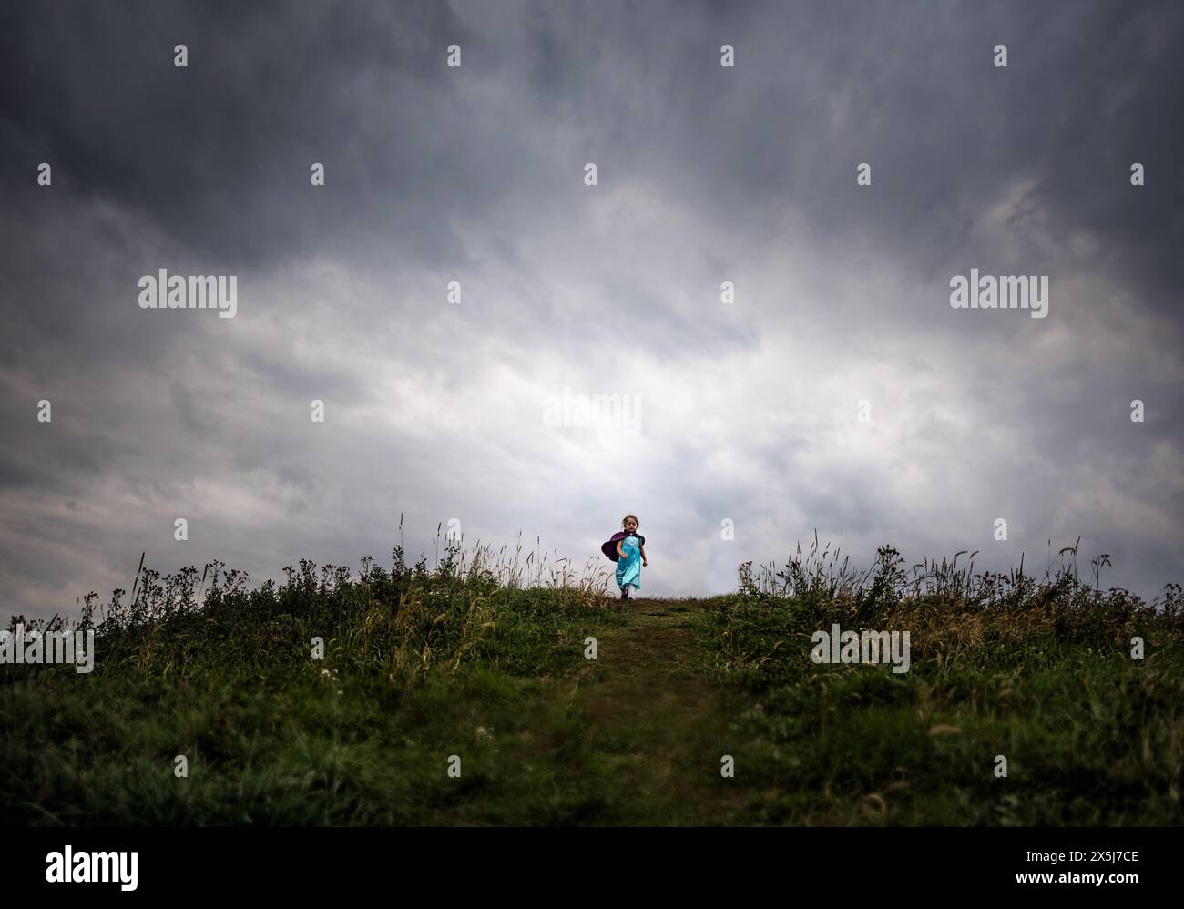 Giovane ragazza che corre in discesa con mantello viola sotto il cielo nuvoloso Foto Stock