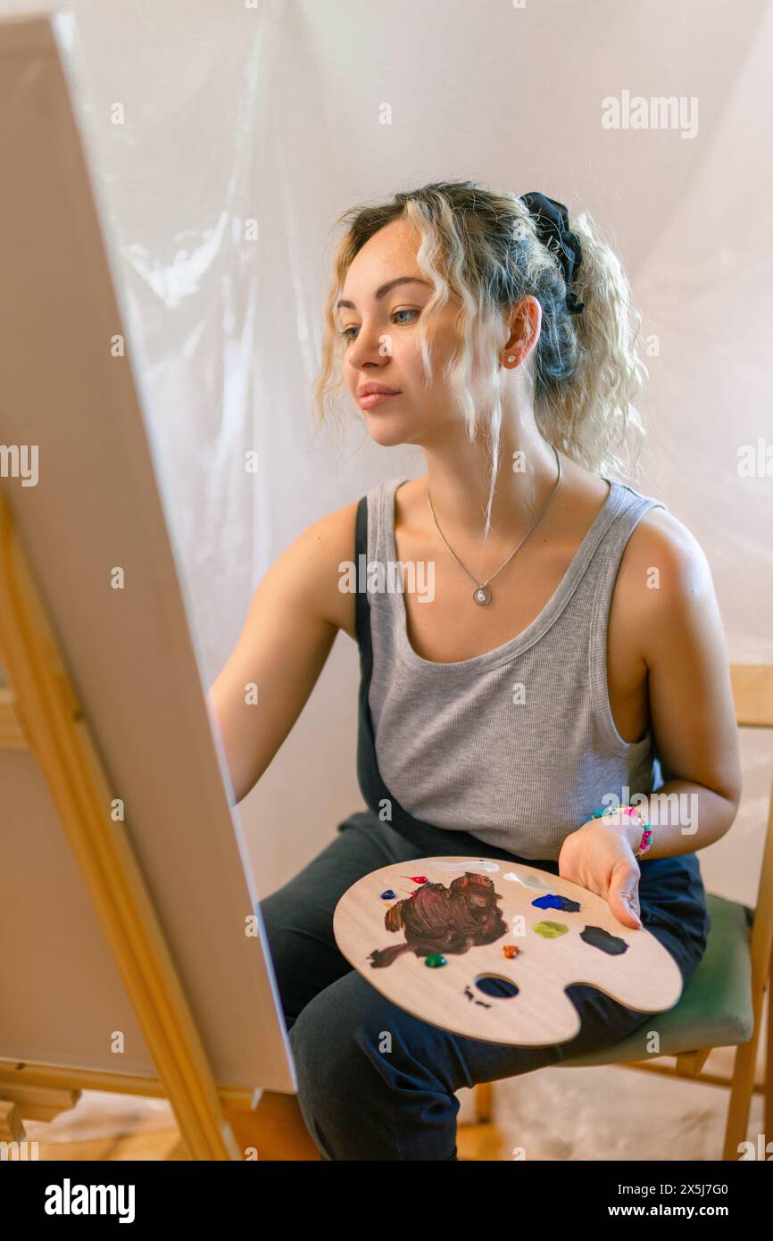 Soddisfatto artista femminile in posa vicino a nuova foto accanto al cavalletto Foto Stock