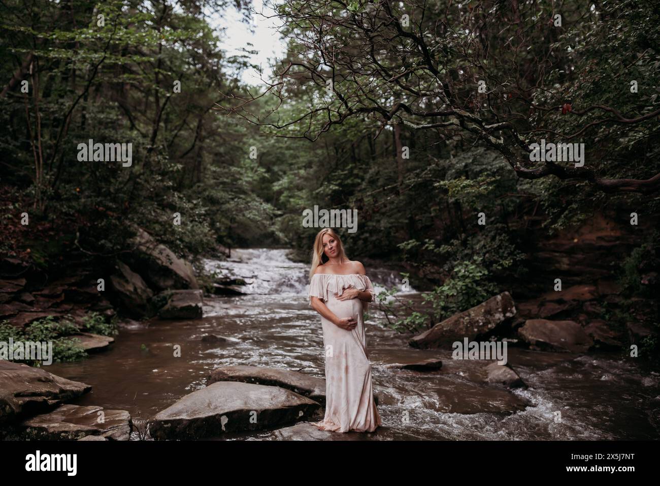Donna incinta del terzo trimestre in piedi nel fiume Foto Stock