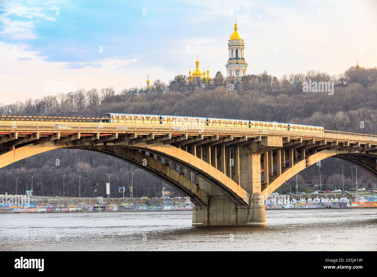 Ucraina, Kiev, Kiev. Ponte della metropolitana sul fiume Dnieper. Tetti del Monastero delle grotte (Pechersk Lavra) sullo sfondo. Foto Stock