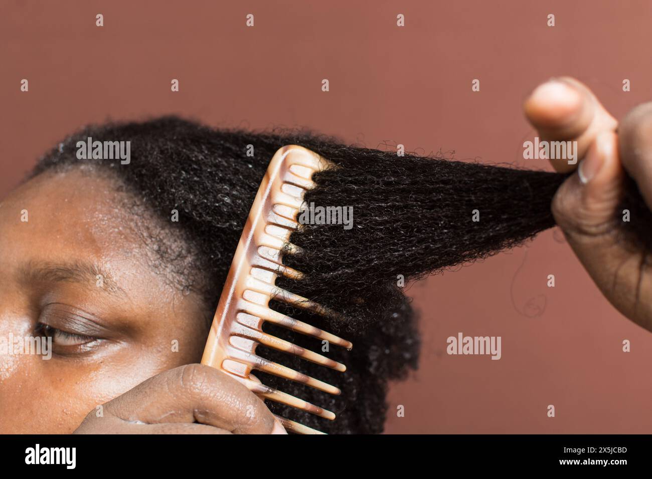 Pettinare i capelli neri ricci con restringimento, utilizzando un pettine a denti larghi per deformare i capelli di tipo 4c bagnati Foto Stock