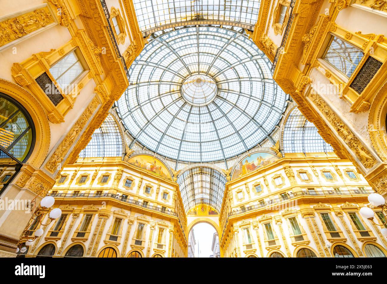 Una squisita cattura della Galleria Vittorio Emanuele II a Milano, Italia. L'immagine mostra l'intricato soffitto a cupola di vetro, circondato da un'architettura dorata ornata, che riflette la grandezza di questo monumento storico Foto Stock