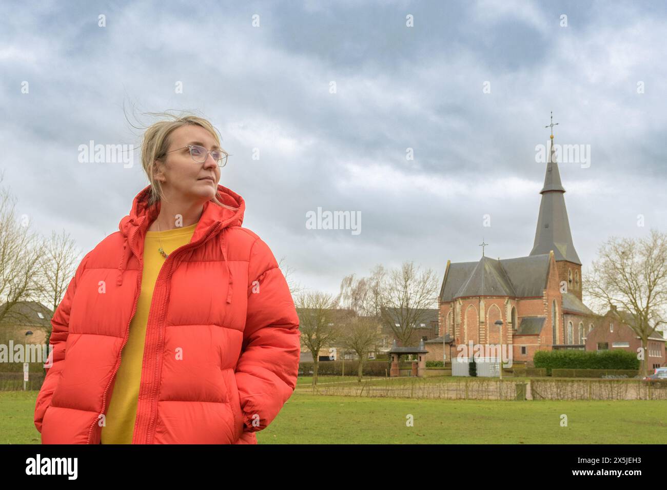 Raffreddamento autunnale. Una donna di mezza età sullo sfondo di un paesaggio europeo autunnale fuori città. Sullo sfondo di una chiesa e di una cl Foto Stock