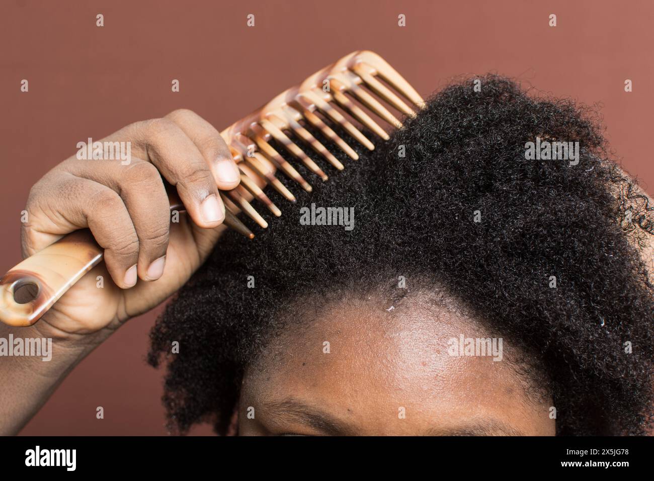 Pettinare i capelli neri ricci con restringimento, utilizzando un pettine a denti larghi per deformare i capelli di tipo 4c bagnati Foto Stock