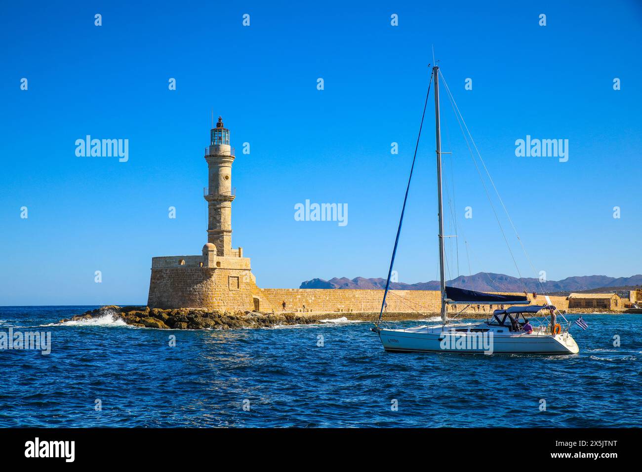 Chania, Grecia. Naviga davanti al faro di Chania in pietra calcarea in una barca a vela sulla baia. (Solo per uso editoriale) Foto Stock