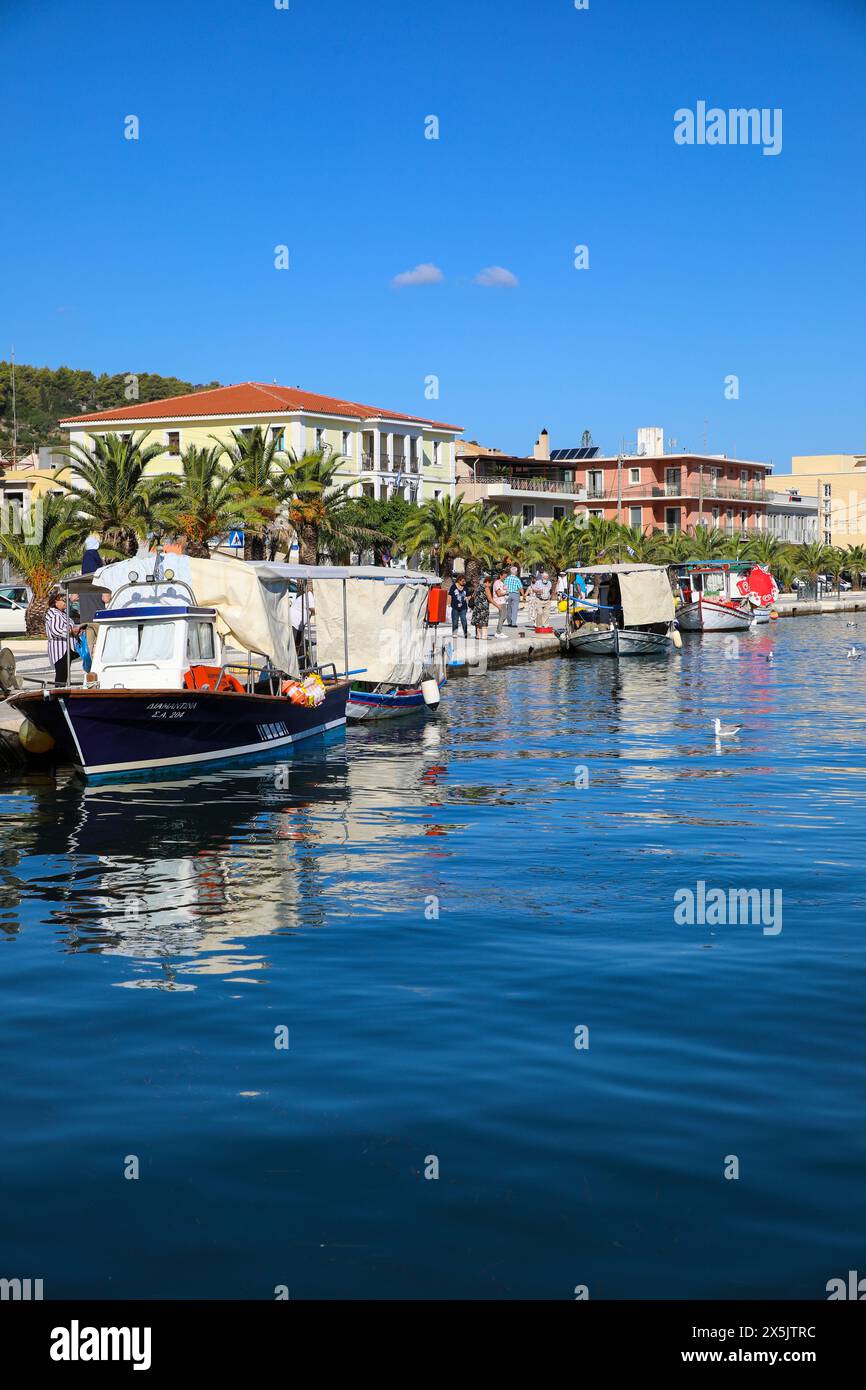 Argostoli, Grecia. Baia sul lungomare, barche, turisti, tetti di tegole rosse, edifici mediterranei e palme. (Solo per uso editoriale) Foto Stock