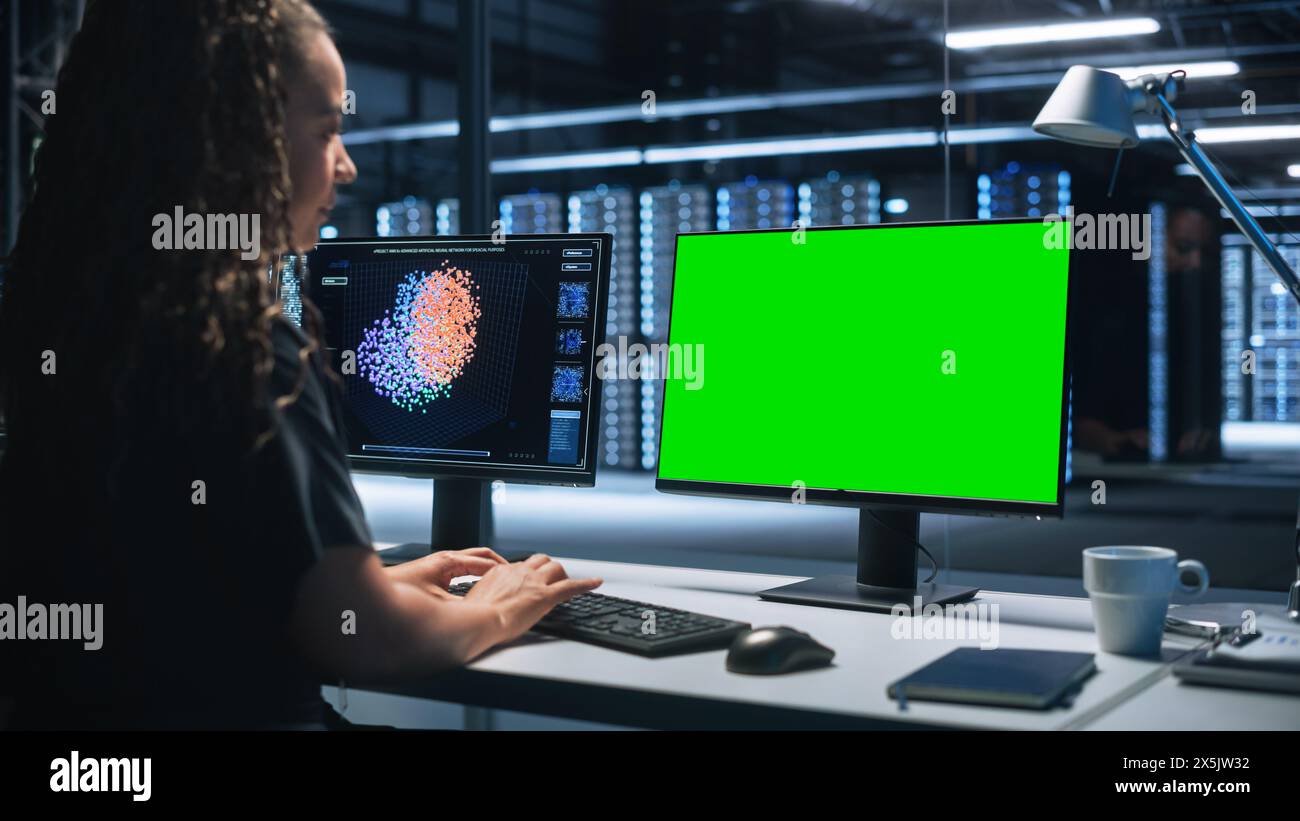 Smart Female IT Programer che lavora su un computer desktop con schermo di occultamento verde nella sala di controllo del sistema del data center. Programmazione professionale codice sofisticato in un laboratorio di sviluppo High Tech. Foto Stock