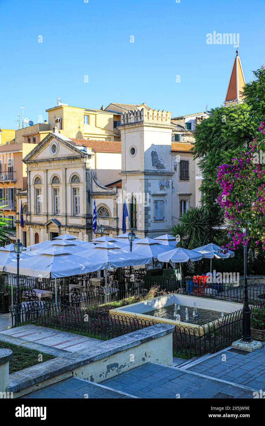 Corfù, Grecia. La città vecchia di Corfù con un castello come una chiesa, caffetterie con ombrelloni e bouganville rosa Foto Stock