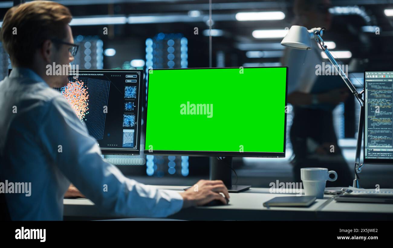 Specialista del supporto tecnico IT professionale e sviluppatore di software che lavora su computer con display Green Screen Mock Up nella sala di controllo di monitoraggio con schermi digitali. Foto Stock