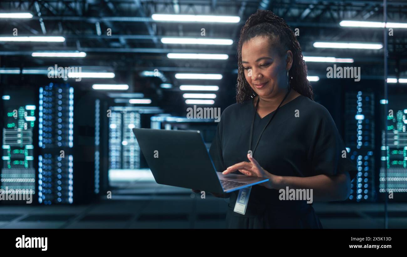 Ritratto di una donna nera specialista che utilizza un notebook nei big data center. L'amministratore delegato lavora con attenzione. Innovazione tecnologica. Concetto di progresso e innovazione Foto Stock