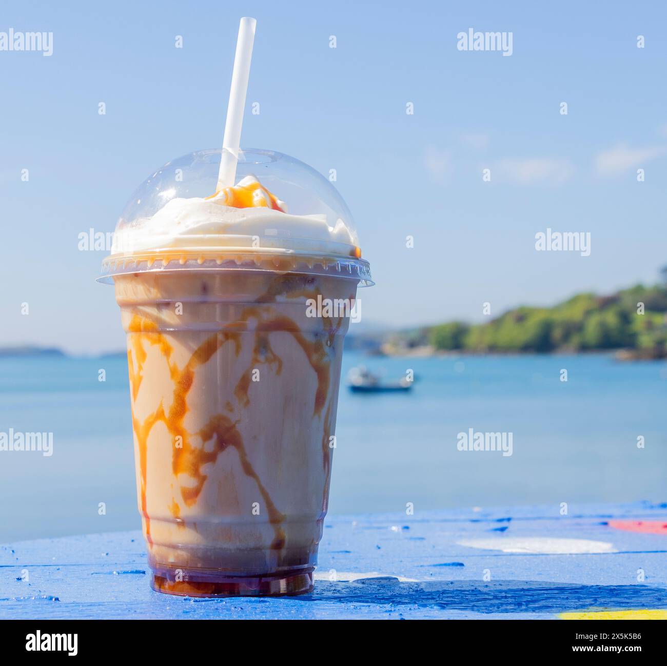 Caffè ghiacciato Caramel vicino al mare sullo sfondo Foto Stock