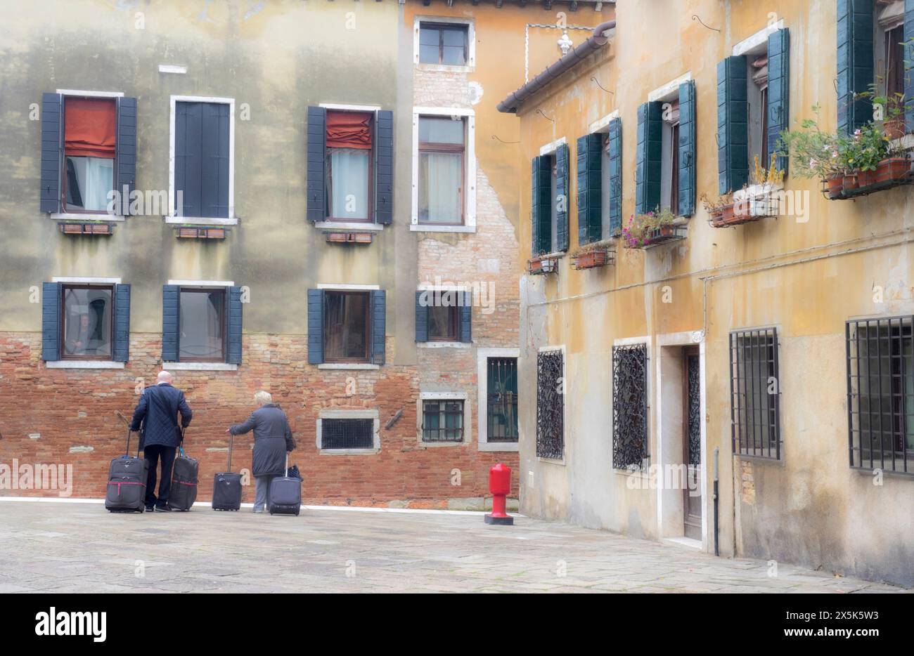 Italia, Venezia. Architettura di Venezia, colorati appartamenti veneziani tradizionali che si affacciano su un canale e turisti con bagagli in attesa di una gondola. (Solo per uso editoriale) Foto Stock