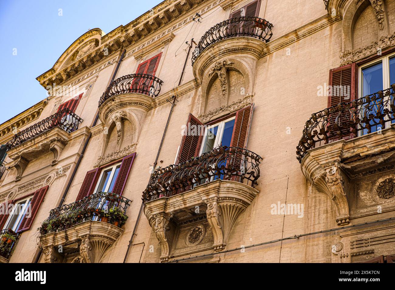 Palermo, Sicilia, Italia. I balconi in stile barocco con persiane rosse si affacciano sull'antico edificio italiano Foto Stock