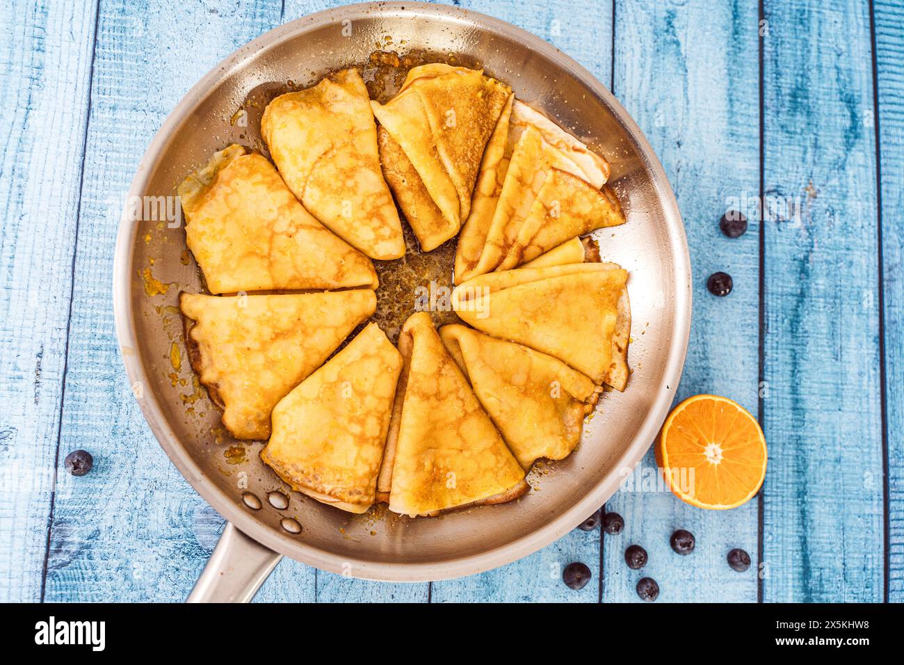 Pancake crepe suzette in una padella su un tavolo di legno. accanto all'arancia tagliata in padella e ai mirtilli. Foto di alta qualità Foto Stock