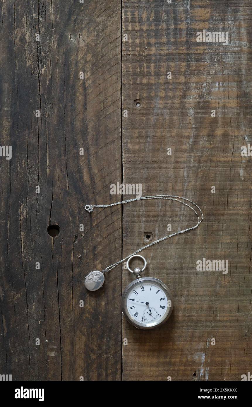 Un vecchio orologio da tasca in argento e un ciondolo d'argento adagiato su vecchie tavole di legno e sul piano del tavolo. copertina libro still life style. Foto Stock