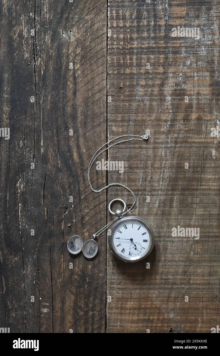 Un vecchio orologio da tasca in argento e un ciondolo d'argento adagiato su vecchie tavole di legno e sul piano del tavolo. copertina libro still life style. Foto Stock