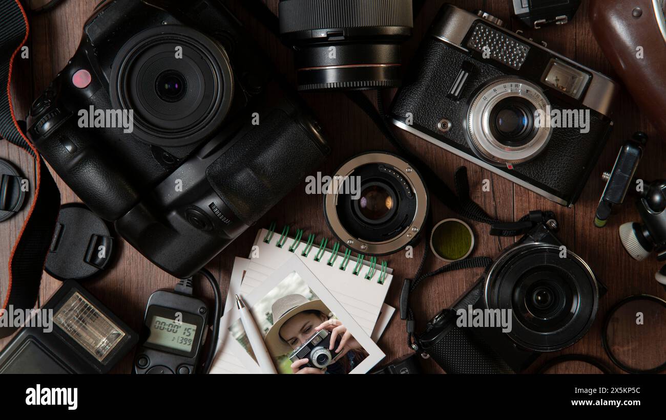 Vista dall'alto della fotografia di una giovane donna che scatta una foto, circondata da flash, filtri, obiettivi, fotocamere moderne e vecchie su un tavolo di legno Foto Stock