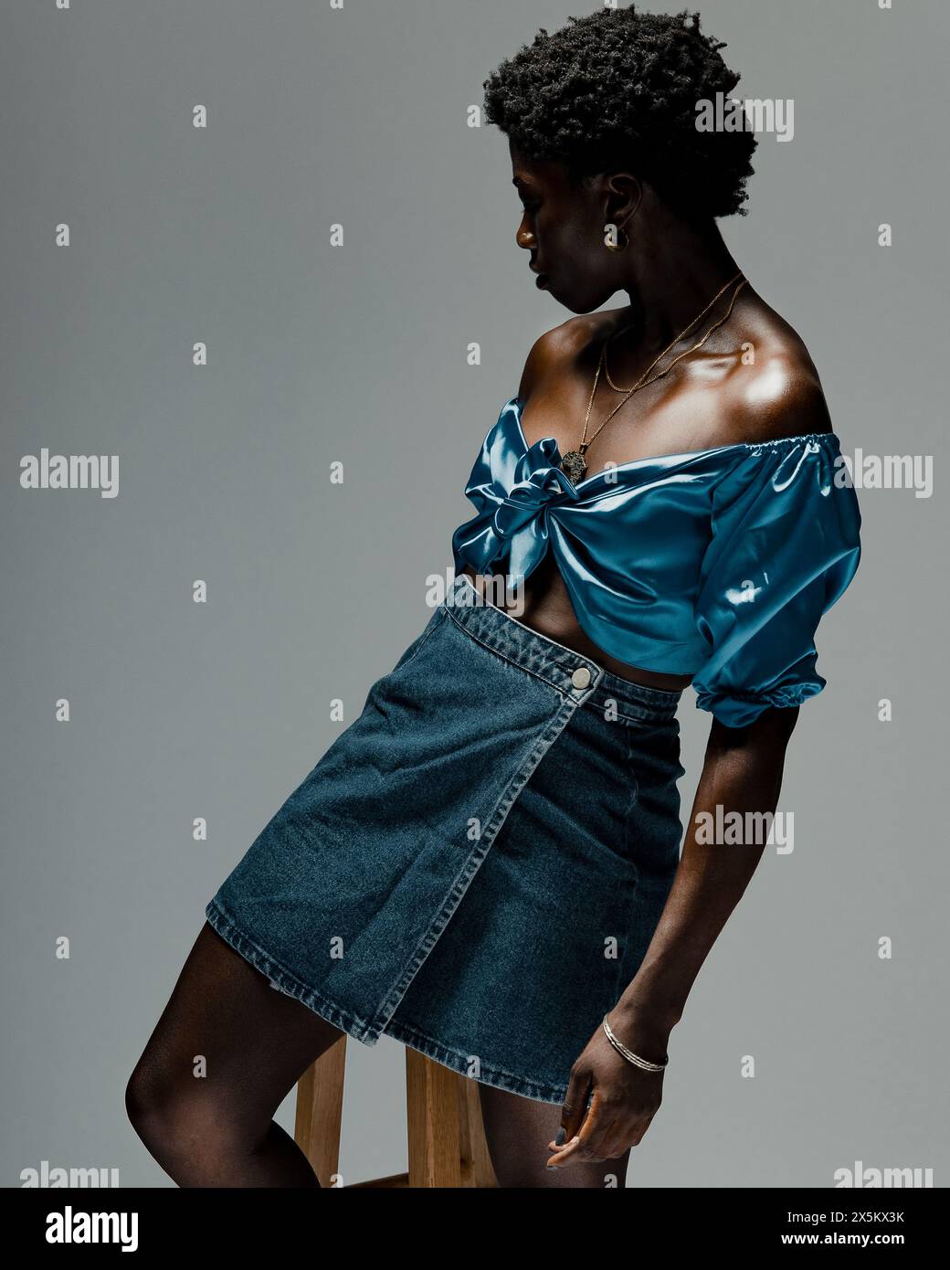 Foto in studio di una giovane donna con top in seta blu e minigonna in denim Foto Stock