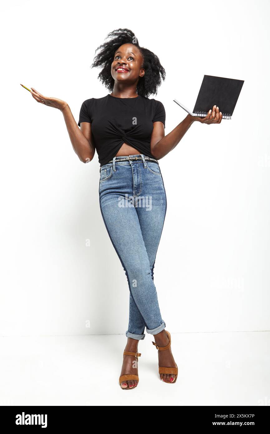Studio ha scattato una donna con t-shirt nera e jeans con taccuino e matita Foto Stock