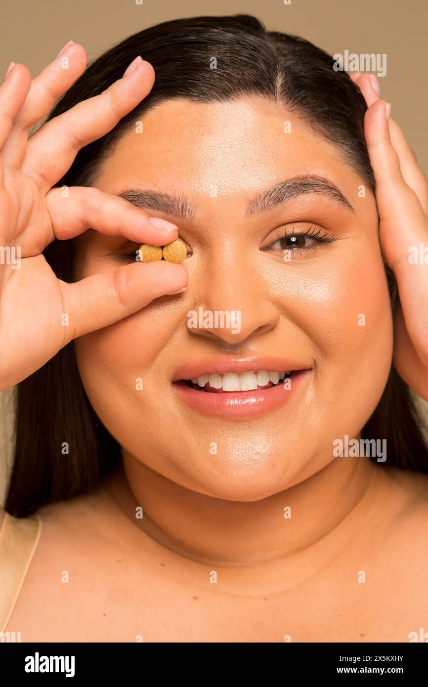 Ritratto in studio di una donna sorridente che tiene due pillole davanti all'occhio, colpo alla testa Foto Stock