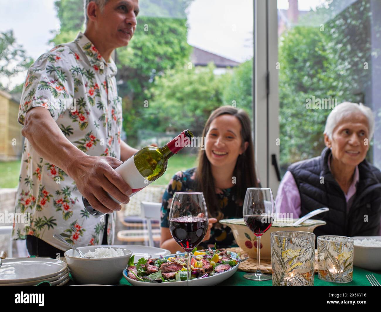 Uomo che versa vino rosso alla cena di famiglia Foto Stock