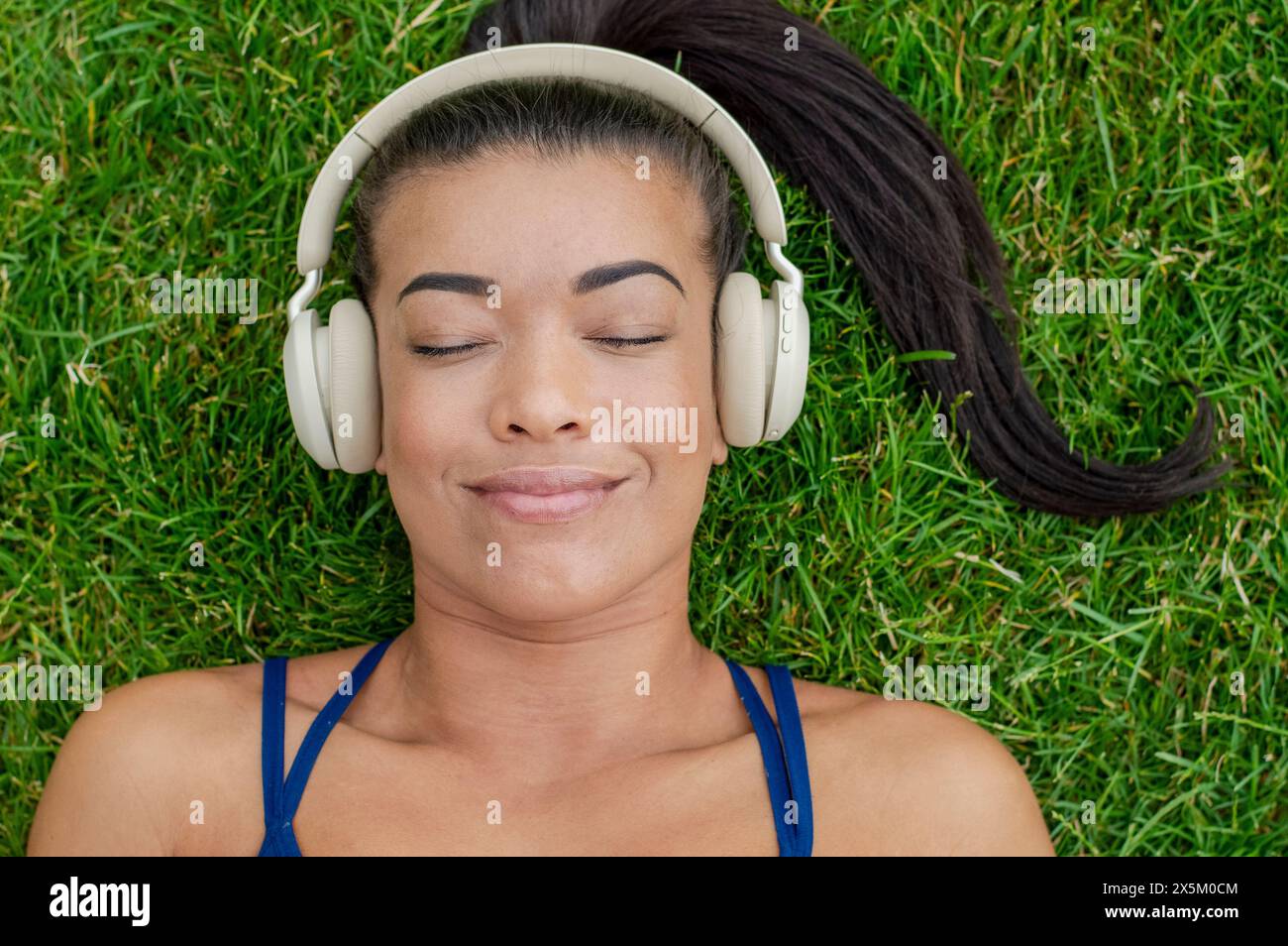 Donna con le cuffie stesa sull'erba Foto Stock
