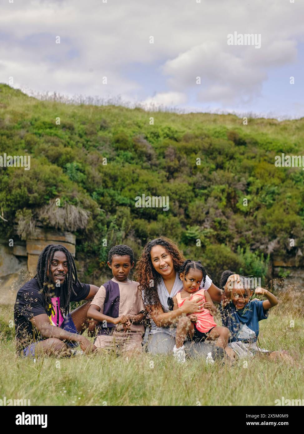 Ritratto all'aperto di una famiglia con tre bambini seduti in erba Foto Stock