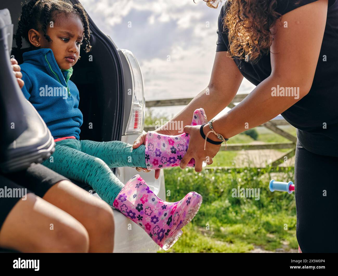 Madre che mette le scarpe di gomma sulla figlia Foto Stock