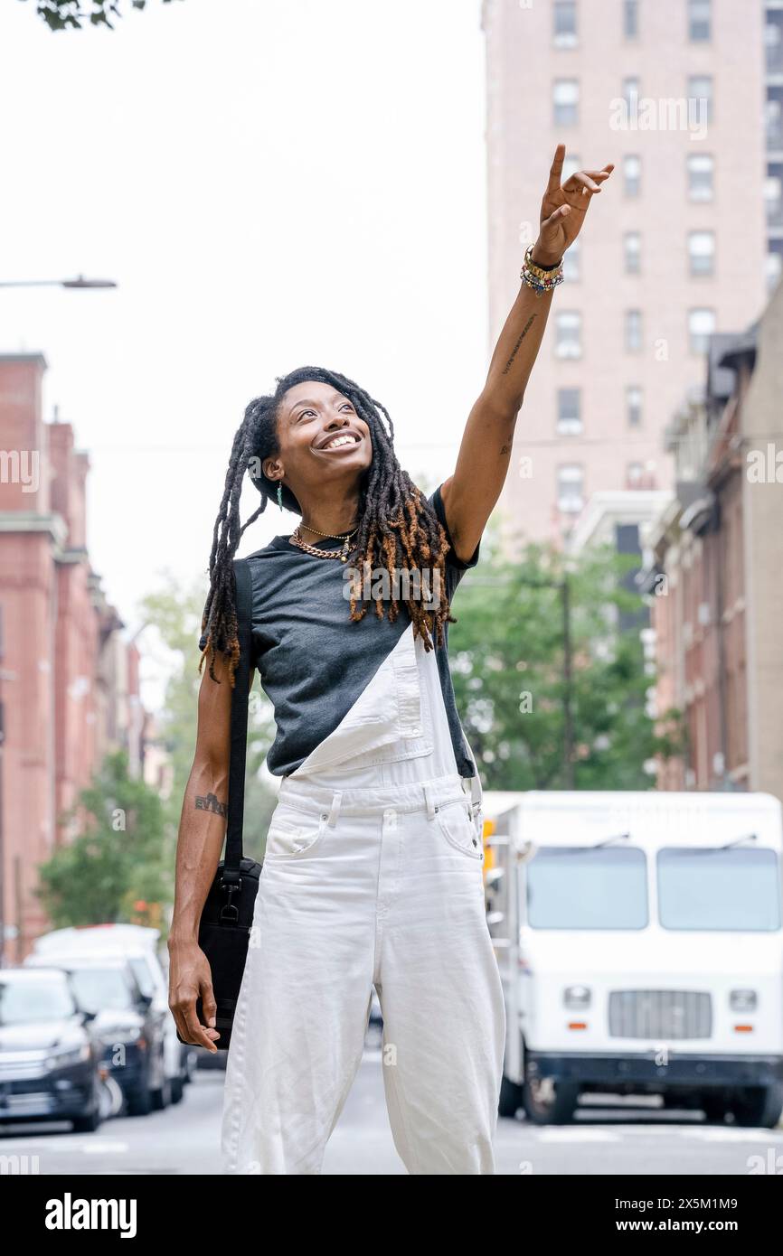 USA, giovane donna sorridente con il braccio sollevato per strada Foto Stock