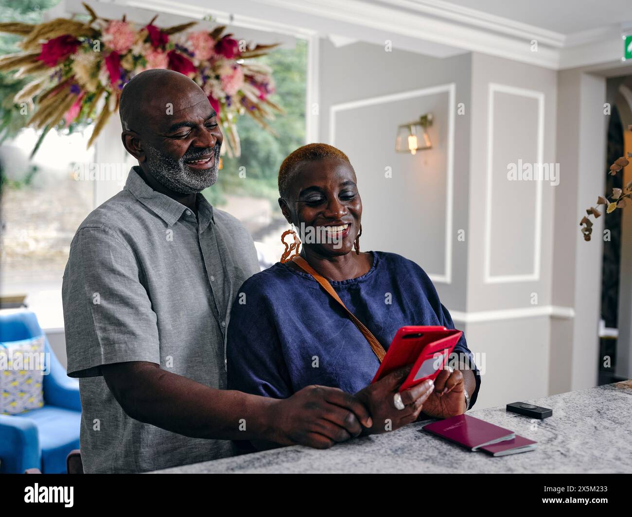 Regno Unito, una coppia matura sorridente che guarda uno smartphone alla reception dell'hotel Foto Stock