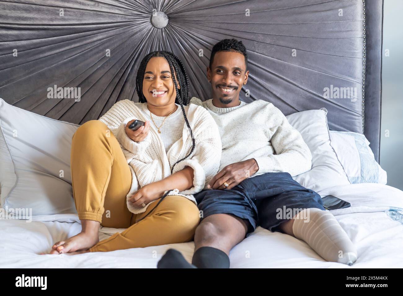 Donna e uomo con una gamba protesica che guardano la TV in camera da letto Foto Stock