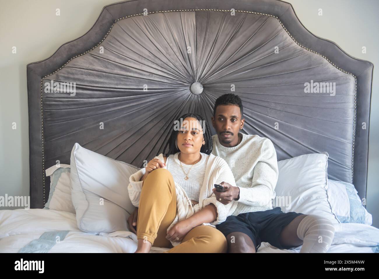 Donna e uomo con una gamba protesica che guardano la TV in camera da letto Foto Stock