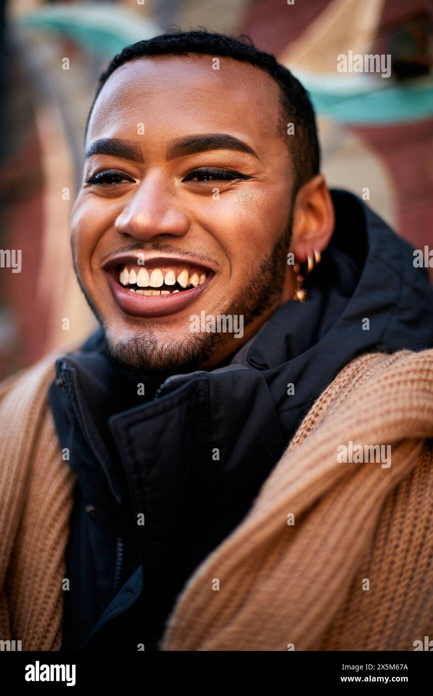 Ritratto di un uomo queer sorridente in giacca e sciarpa Foto Stock