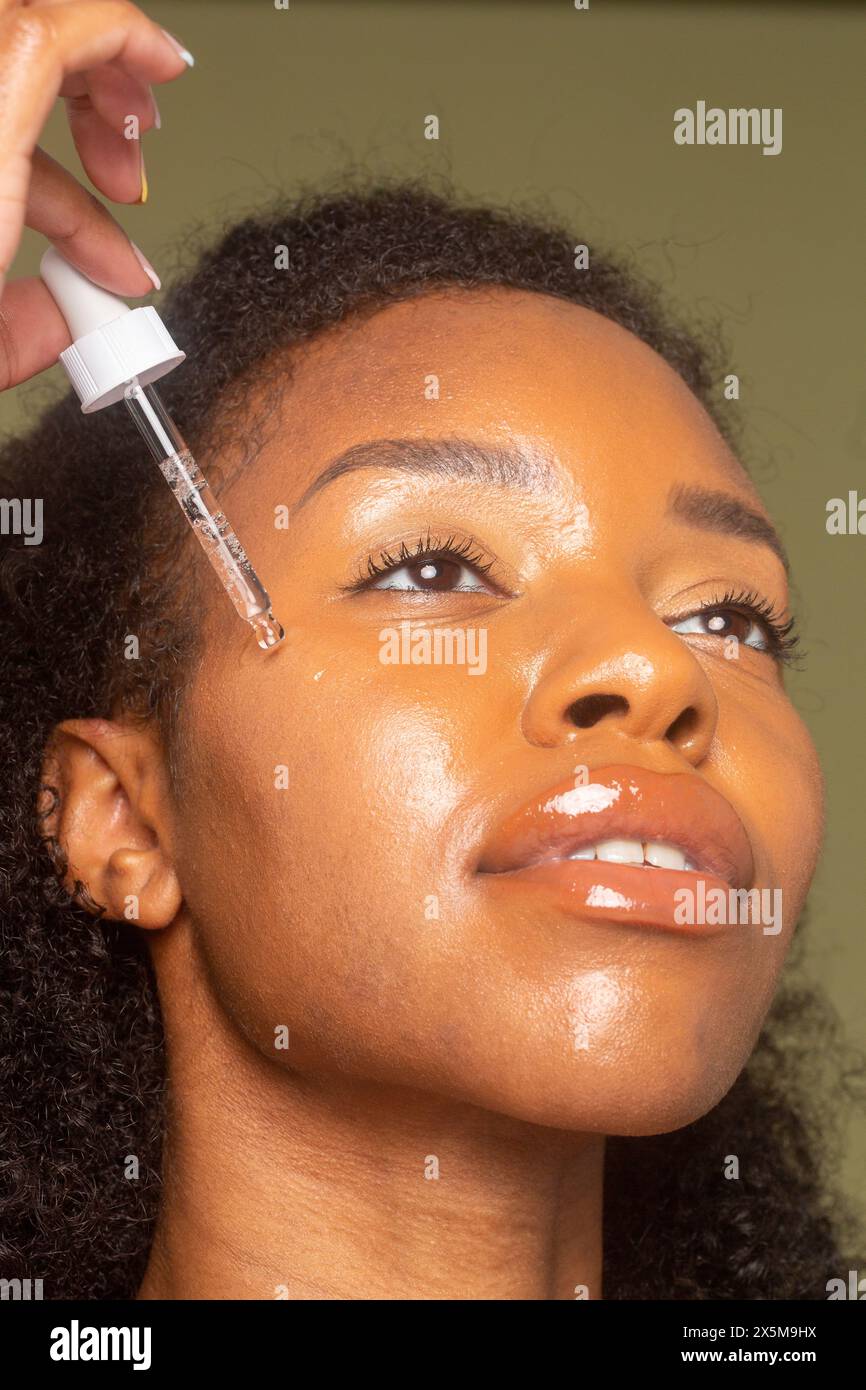 Primo piano di una donna che fa cadere l'olio facciale sul viso Foto Stock