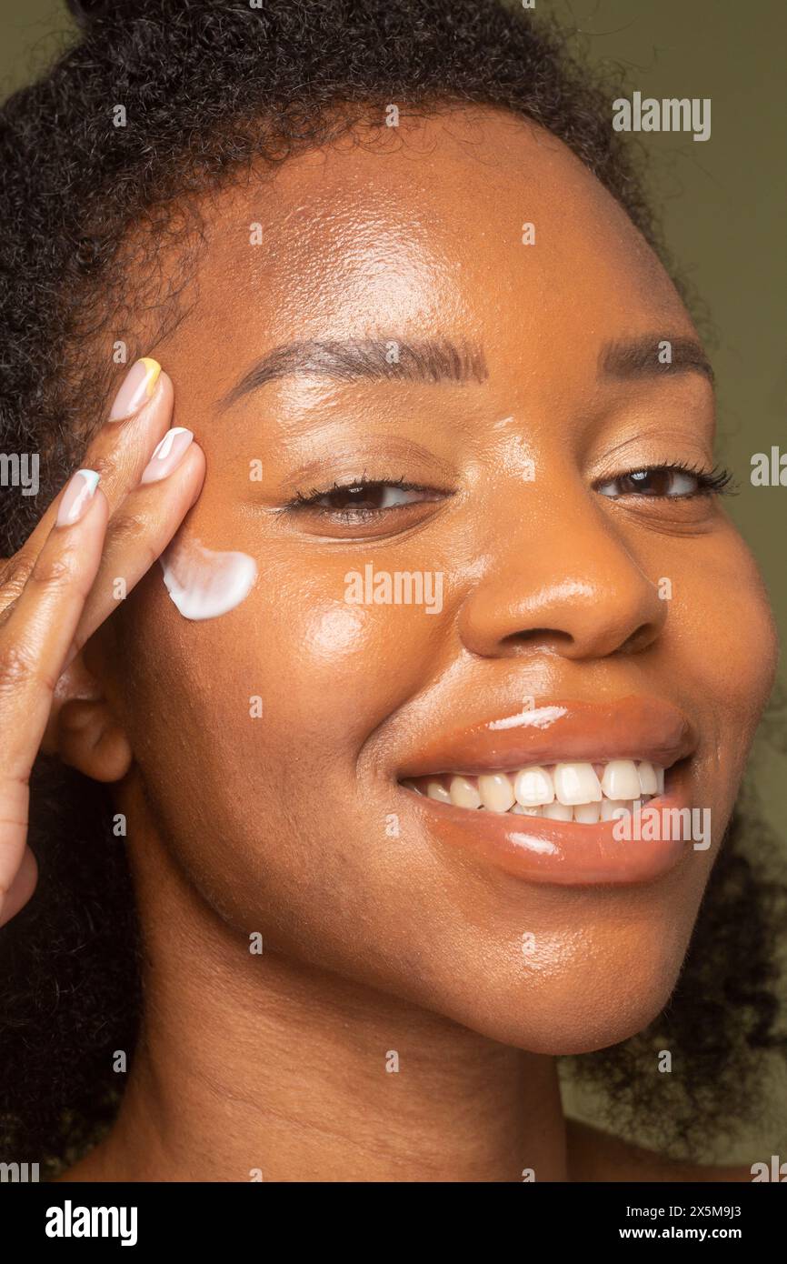 Primo piano di una donna sorridente che applica la crema sul viso Foto Stock