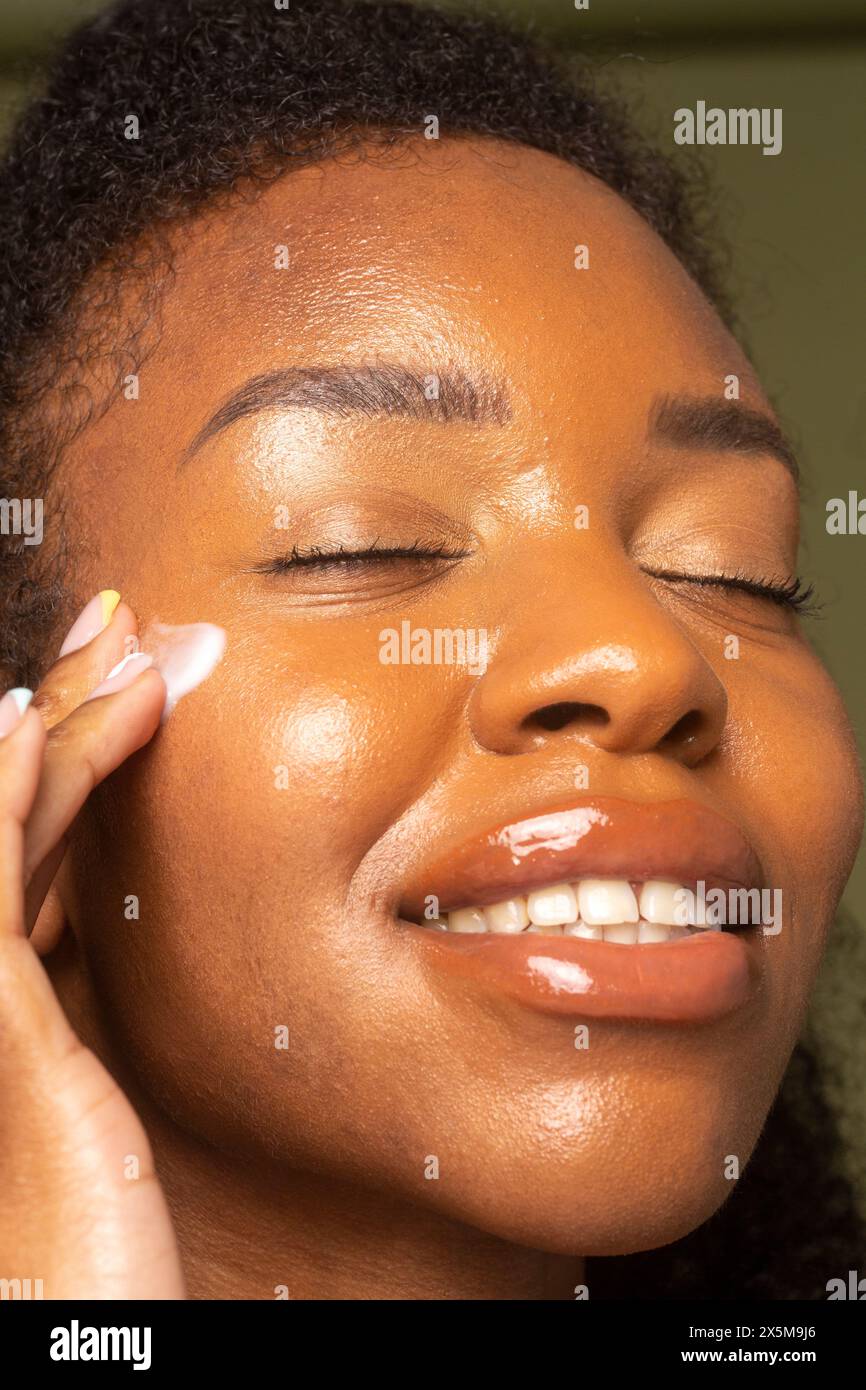 Primo piano di una donna sorridente che applica la crema sul viso Foto Stock