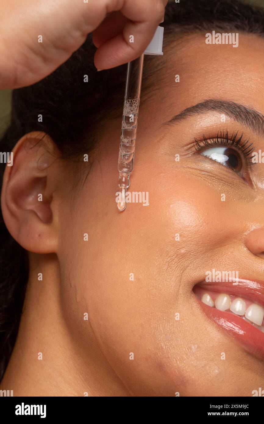 Primo piano di una donna che fa cadere l'olio facciale sul viso Foto Stock
