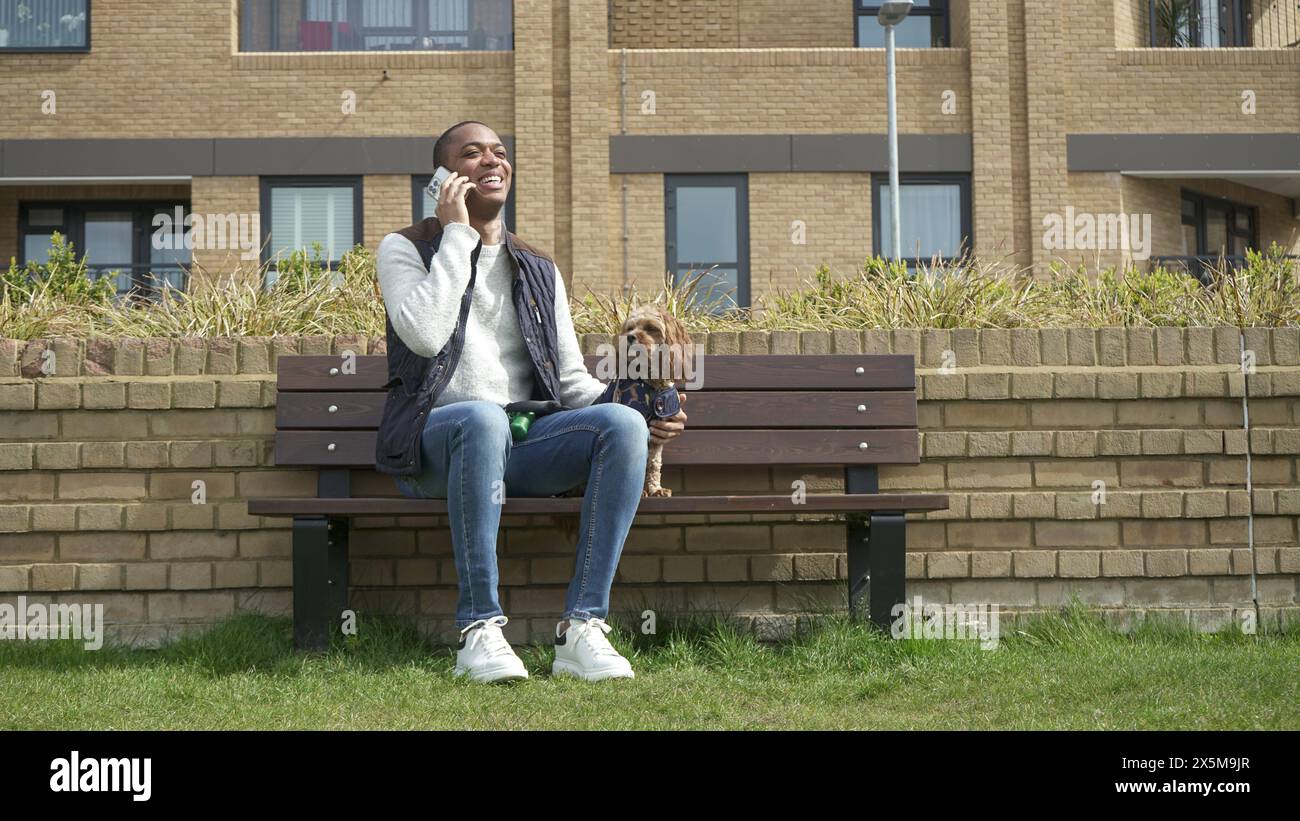 Uomo con cane seduto sulla panchina del parco Foto Stock