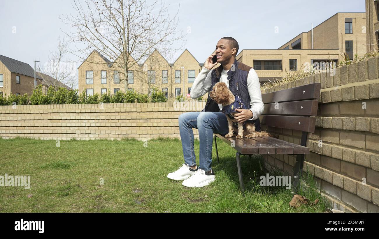 Uomo con cane seduto sulla panchina del parco Foto Stock