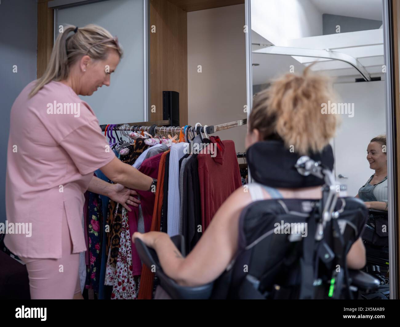 Assistente che aiuta la donna in sedia a rotelle a scegliere i vestiti Foto Stock