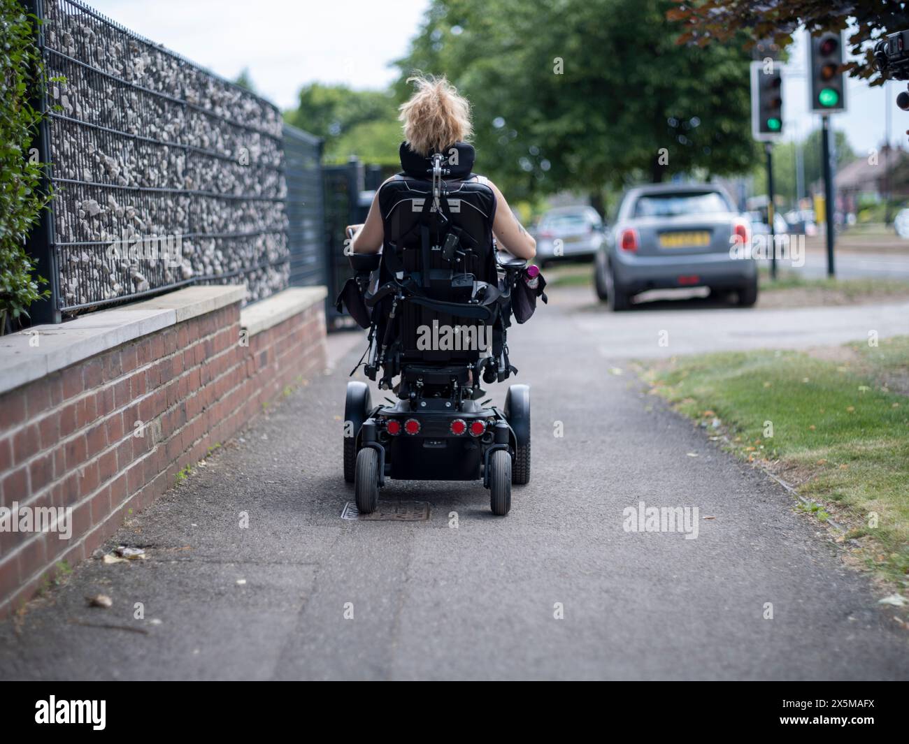 Donna in sedia a rotelle elettrica che va a piedi Foto Stock