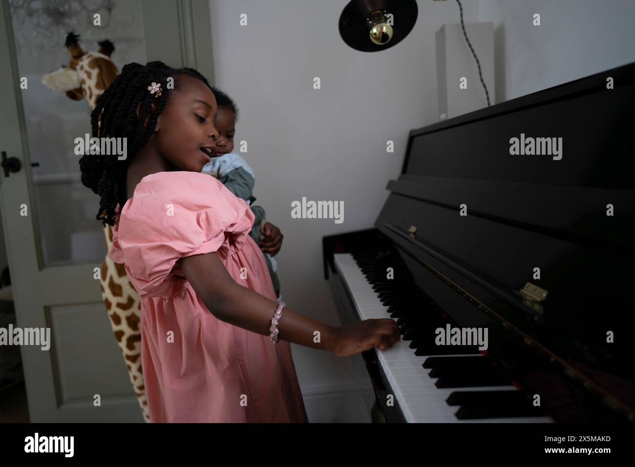 Ragazza (6-7) che tiene in mano il fratellino (2-5 mesi) e suona il pianoforte Foto Stock