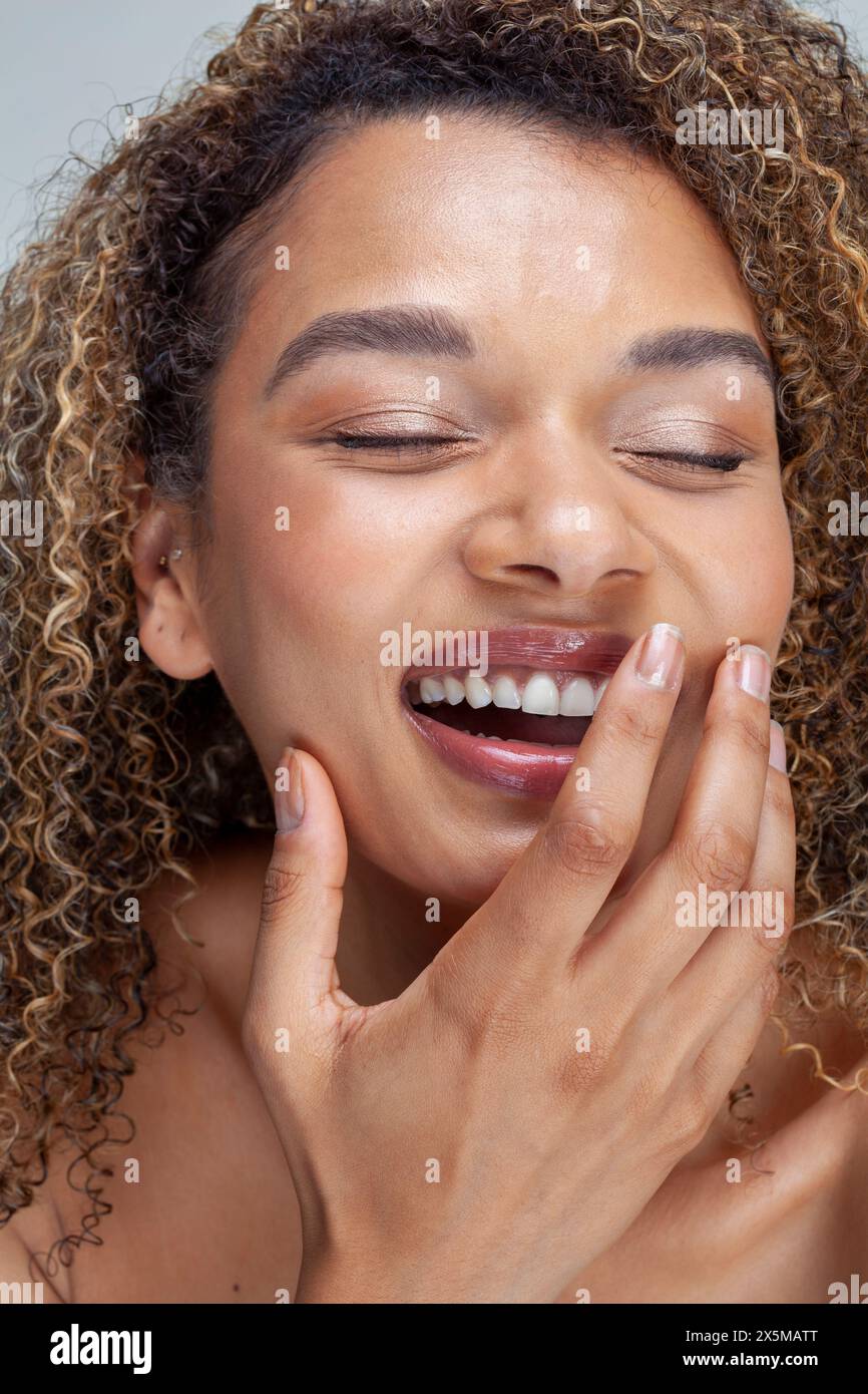 Primo piano di una donna sorridente con capelli ricci e occhi chiusi Foto Stock