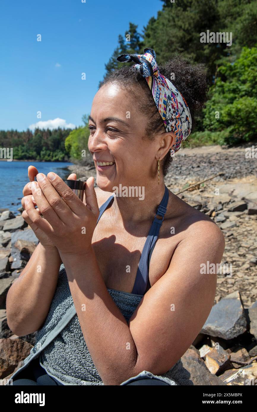 Donna sorridente che si gusta il tè sulla riva del lago, Yorkshire, Regno Unito Foto Stock