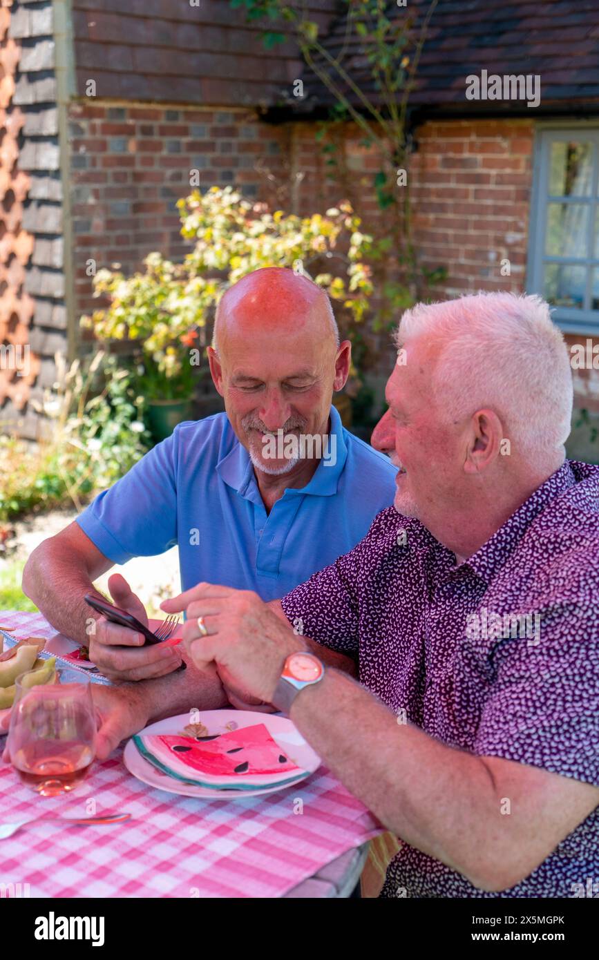 Coppia di uomini anziani che si rilassano in giardino e utilizzano il telefono Foto Stock