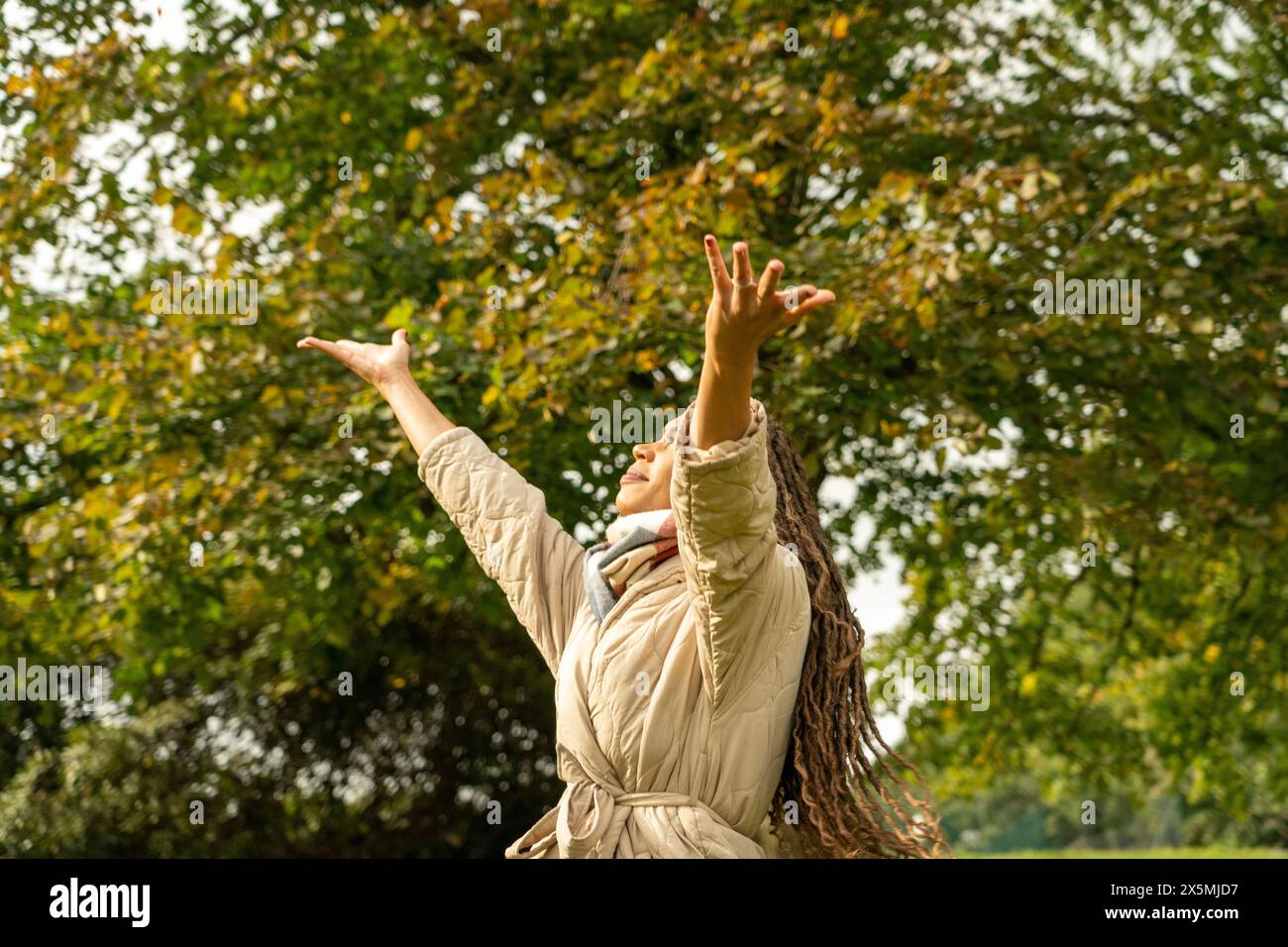 Donna sorridente con le braccia sollevate nel parco in autunno Foto Stock