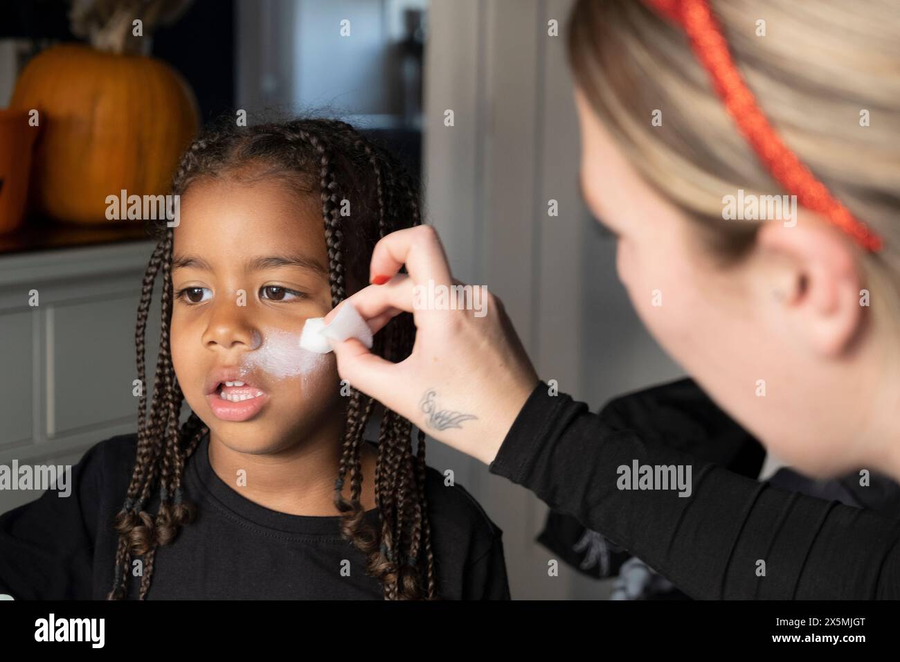 Primo piano di una donna che applica vernice bianca sul viso dei figli per Halloween Foto Stock