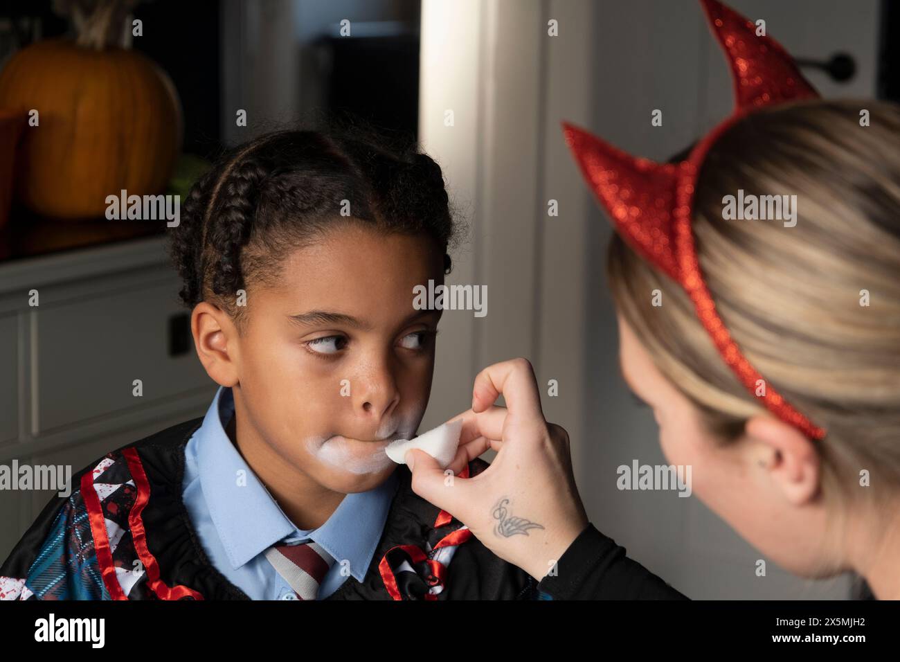 Primo piano di una donna che applica vernice bianca sul viso dei figli per Halloween Foto Stock
